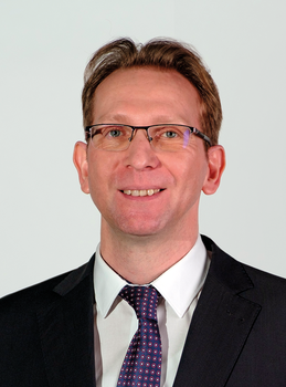 Formális öltözet üzleti viseletben Sötét öltöny, fehér ing és mintás nyakkendő formális öltözetben.