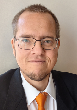 Egy személy formális öltözetben, fehér inggel és narancssárga nyakkendővel