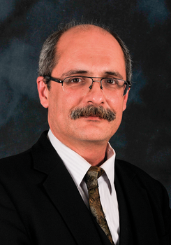 Formális öltözetben lévő személy fekete zakóval, fehér inggel és mintás nyakkendővel.