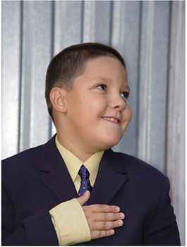 Formális öltözet sötétkék zakóval és kék nyakkendővel Személy formális öltözetben, sötétkék zakóval, világos sárga inggel és kék nyakkendővel, fémes háttér előtt.