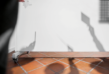 Gurulós tábla fehér fal előtt, különböző árnyékokkal, például kéz és téglalap alakú tárgy árnyéka.