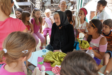Gyerekek egy kézműves foglalkozáson vesznek részt, ahol textilből készítenek tárgyakat, körülöttük színes anyagok és eszközök láthatók.