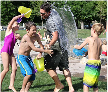 Gyerekek vizes játéka a parkban Gyerekek vizes vödrökkel játszanak egy parkban, nyári szórakozás.