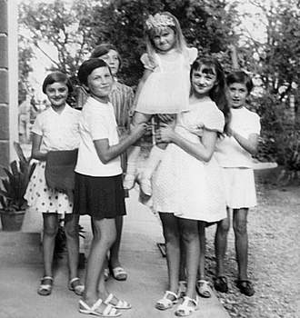 Gyerekek csoportképe nyári ruhában Hat gyerek látható, akik közül az egyik kislányt a többiek felemelik, nyári ruhában, fák háttérben.