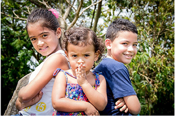 Gyerekek a parkban Három gyerek egymás mellett áll egy parkban, háttérben fák láthatók.