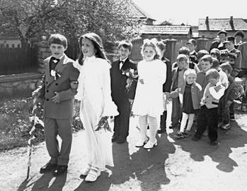 Gyerekek ünnepi ruhában egy szabadtéri eseményen Csoport gyerekek ünnepi ruhában állnak egy szabadtéri helyszínen, valószínűleg egy ünnepi eseményen vagy felvonuláson.