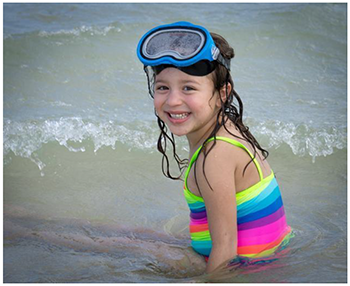 Gyermek a tengerparton búvárszemüvegben Gyermek színes fürdőruhában ül a tengerparton, búvárszemüveget viselve.