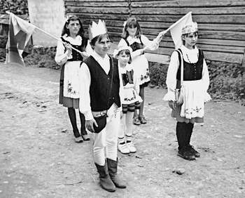 Gyermekek népviseletben zászlókkal Négy gyermek hagyományos népviseletben, zászlókkal a kezükben, vidéki környezetben.