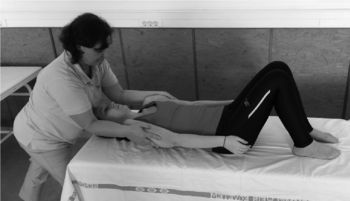 Gyógytornász segít egy páciensnek gyógytorna gyakorlatot végezni egy kezelőágyon.