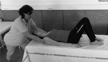 Gyógytornász nyak kezelést végez egy fekvő páciensen, aki egy kezelőágyon fekszik.