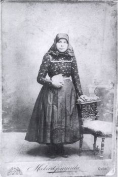 Hagyományos magyar népviseletbe öltözött nő Győrben Egy hagyományos magyar népviseletbe öltözött nő látható, aki egy díszes székre támaszkodik. A kép alján a 'Makanitzyné' és 'Győr' feliratok olvashatók.