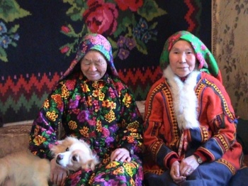 Hagyományos ruhába öltözött nők kutyával Két hagyományos ruhába öltözött nő kutyával, virágmintás háttér előtt.