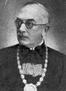 Hivatalos öltözet díszes lánccal és kitüntetéssel Hivatalos öltözet, amely egy díszes láncot és egy kitüntetést tartalmaz.