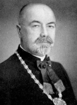 Hivatalos öltözetben lévő személy díszes lánccal Egy hivatalos öltözetben lévő személy látható, nyakában díszes lánccal.