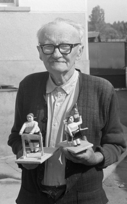 Idős férfi két kézzel készített, festett fa figurát tart a kezében.