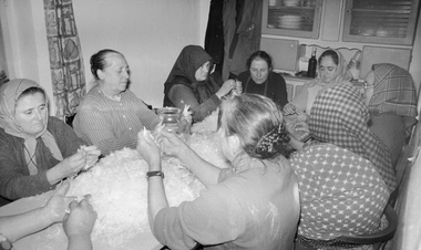 Idős asszonyok tollat fosztanak egy asztal körül ülve, hagyományos tevékenység közösségi munka keretében.