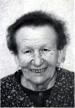 Idős nő mintás ruhában és fülbevalóval Idős nő sötét, mintás ruhában, fülbevalóval, homályosított arccal.