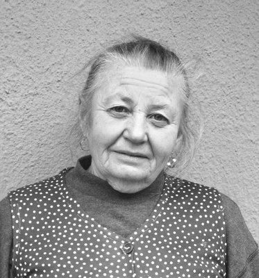 Idős nő pöttyös ruhában, szürke háttér előtt, fekete-fehér kép