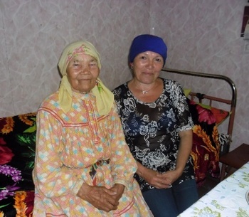 Idős nők ülnek egy ágyon egy szobában Két idős nő ül egy ágyon egy szobában, virágos takaróval és kendővel.