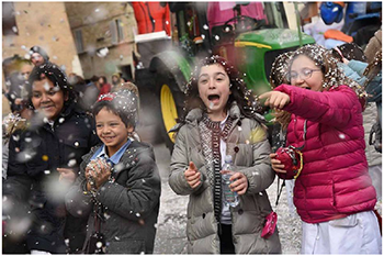 Karneváli jelenet gyerekekkel és konfettivel Gyerekek karneváli hangulatban konfettivel játszanak, háttérben egy traktor.