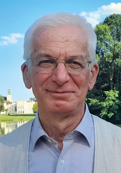 Kastély a tó partján, háttérben fák és kék ég látható a képen.