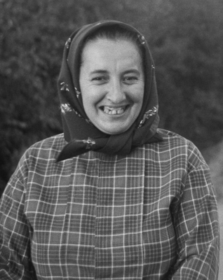 Kendőt viselő személy kockás mintás ruhában, háttérben természetes környezet.