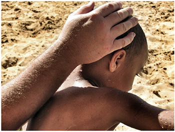 Kéz simogatja gyerek fejét a tengerparton Kéz simogatja gyerek fejét a homokos tengerparton, háttérben homok látható.