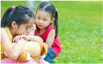 Kislányok játszanak plüssállattal a szabadban Két kislány plüssállattal játszik a zöld fűben, szabadban.