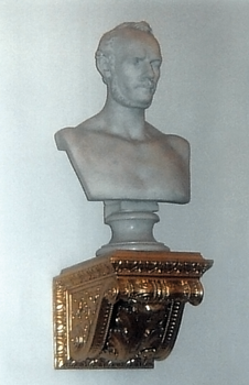 Klasszikus stílusú mellszobor, amely egy díszes arany színű konzolon van elhelyezve.