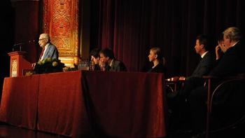 Konferencia vagy előadás pódiumon beszélő személlyel Konferencia vagy előadás, ahol egy személy beszél a pódiumon, több ember ül az asztalnál.