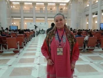 Konferencia résztvevője áll a kamera előtt, háttérben a színpad és a közönség egy impozáns épületben.