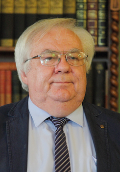 Könyvespolc tele régi könyvekkel, háttérben könyvtári környezet.