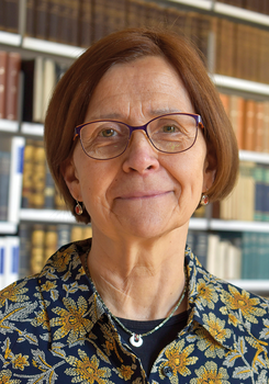 Könyvespolc tele könyvekkel, virágmintás ruhát viselő személy nyaklánccal