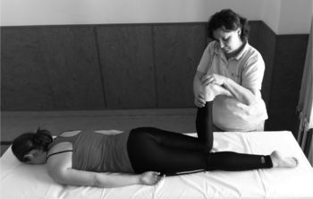 Egy terapeuta masszázs vagy fizioterápiás kezelést végez egy fekvő nő lábán.