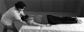 Masszőr hátmasszázst végez egy fekvő személyen, ZÉNÓ felirattal a pólón.