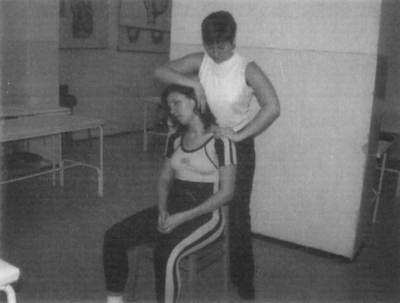 Nyakmasszázs egy széken ülő személynek Egy személy nyakmasszázst kap, miközben egy széken ül, a masszőr állva végzi a kezelést.