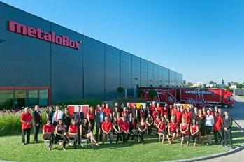 Metalobox cég csapata az épület előtt, háttérben teherautókkal és a cég logójával.