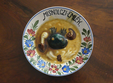 Díszes kerámia tányér 'Miskolczi-emlék' felirattal, virágmintákkal és domború zöld díszítéssel.