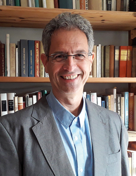 Mosolygó férfi könyvespolc előtt Mosolygó férfi áll egy könyvespolc előtt, tele könyvekkel