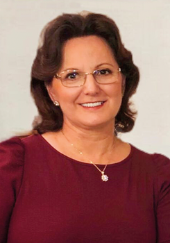 Nő bordó ruhában, arany nyaklánccal és medállal, háttérben semleges szín