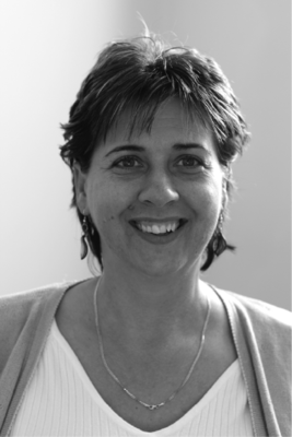 Nő fehér felsőben és kardigánban, nyaklánccal, rövid hajjal