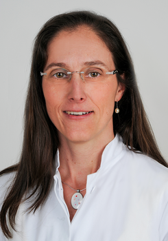 Nő fehér orvosi köpenyben, nyakában egy medállal.