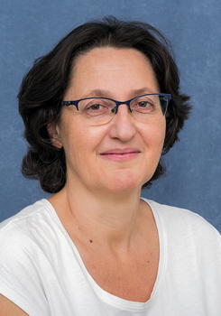 Egy nő fehér pólóban, kék háttér előtt, a képen a nyak és a haj látható.