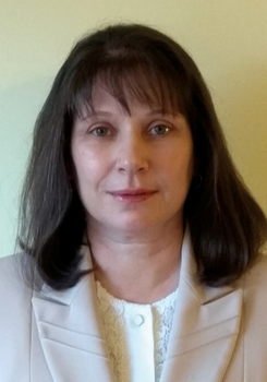 Egy nő világos színű blézert és fehér csipkés blúzt visel.