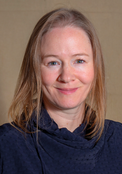 Egy nő világosbarna hajjal és sötétkék ruhában látható a képen.