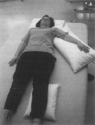 Egy nő fekszik az ágyon, párnákkal megtámasztva a fejét, karját és lábát.