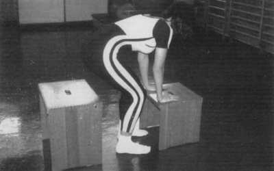 Nő edzőteremben fa dobozra támaszkodva Egy nő edzőteremben gyakorol, két fa dobozra támaszkodva, sportos ruhában.