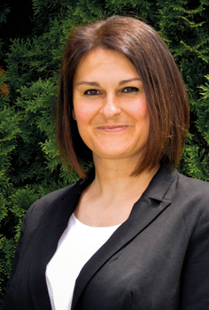 Nő fekete blézerben és fehér felsőben zöld növények előtt Nő fekete blézerben és fehér felsőben, háttérben zöld növényekkel