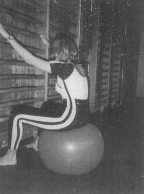 Egy nő ül egy fitnesz labdán a tornateremben, és a bordásfalat fogja.