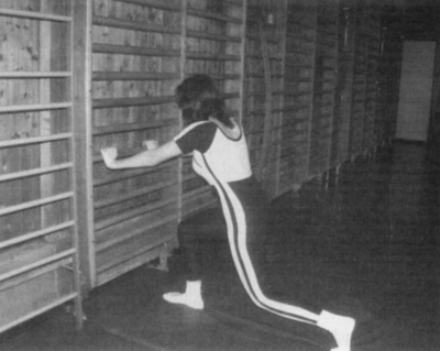 Nő gimnasztikai gyakorlatot végez a bordásfalnál Egy nő gimnasztikai gyakorlatot végez a bordásfalnál, fekete-fehér kép.